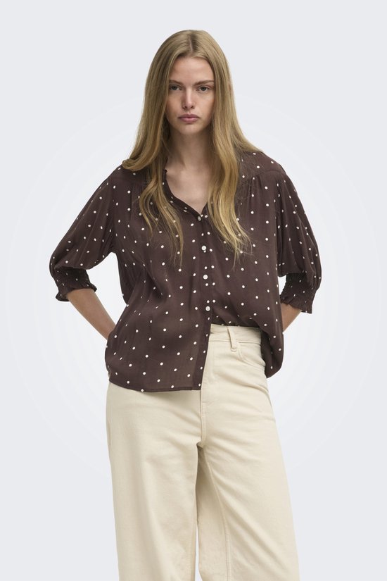Model draagt een bruine blouse met witte stippen en een off-white wijde broek.