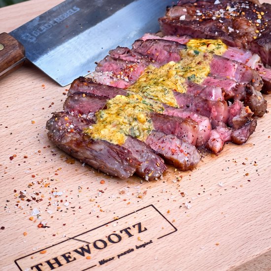 Gegrilde biefstuk, gesneden op een houten plank, bedekt met kruidenboter.