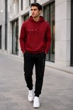 Man draagt bordeauxrode hoodie met 'PARIS'-print en zwarte joggingbroek met 'PARIS'-print.