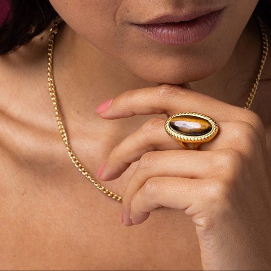 Gouden ring met ovale tijgeroog edelsteen, gedragen door een vrouw met gouden ketting.