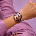 Gouden smartwatch met paarse band om de pols, met een foto van een stel op het scherm.