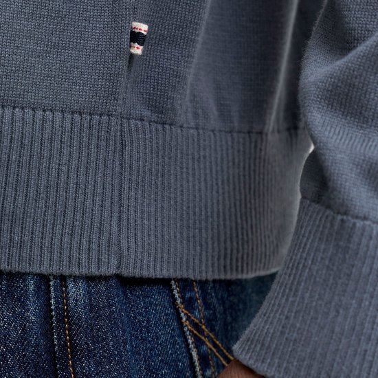 Detail van de zoom en de mouwboord van een grijze gebreide polo.