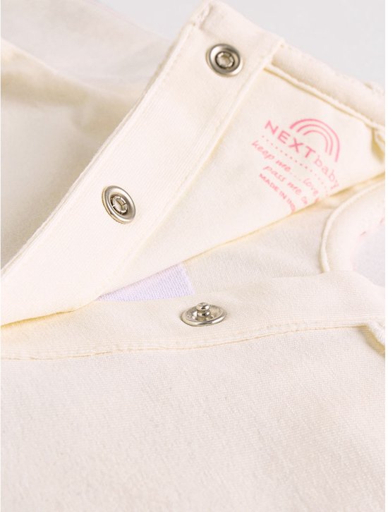 Sluiting van drukknoopjes op een roomwitte longsleeve met Next baby label.