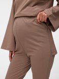 Close-up van een zwangere vrouw in een bruine zwangerschapsbroek met hoge tailleband.