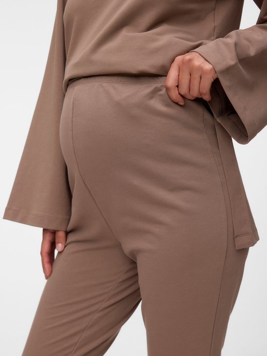 Close-up van een zwangere vrouw in een bruine zwangerschapsbroek met hoge tailleband.