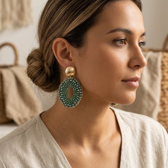 Model met grote, ovale turquoise groene oorbellen met gouden details.