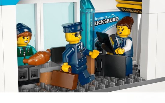 LEGO poppetjes bij een LEGO City luchthavenbalie met bagage en een "Welcome to BRICKSBURG" bord.