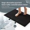 Blote voeten stappen op een zwarte, absorberende badmat. Natte voetafdrukken op de vloer verdwijnen. De tekst "Hoge absorptiecapaciteit" is zichtbaar.