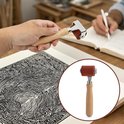 Een hand die een rode rol met een houten handvat vasthoudt, boven een gedrukte afbeelding, met op de achtergrond een werkplek.