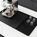 Zwarte mat met een zilverkleurige espressomachine die espresso maakt in een glas, met vier glazen op een afdruiprek.