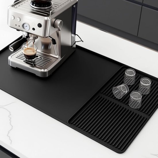 Zwarte mat met een zilverkleurige espressomachine die espresso maakt in een glas, met vier glazen op een afdruiprek.