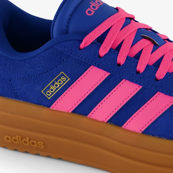 Detail van de zijkant van een blauwe Adidas VL Court Bold damessneaker met roze strepen en een bruine zool.