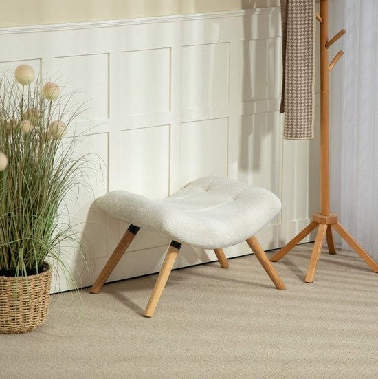 Crèmekleurig, gebogen fleece voetenbankje met houten poten, geplaatst naast een plantenmand en kapstok.