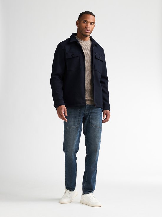 Model draagt een donkerblauw Petrol Industries overshirt over een beige trui en blauwe jeans.