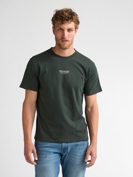 Donkergroen T-shirt met kleine witte tekstprint op de borst. Model draagt een spijkerbroek.