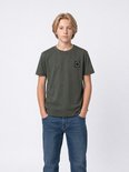 Jongen staat recht vooruit in een donkergroen T-shirt met 'PETROL INDUSTRIES' logo en blauwe jeans.