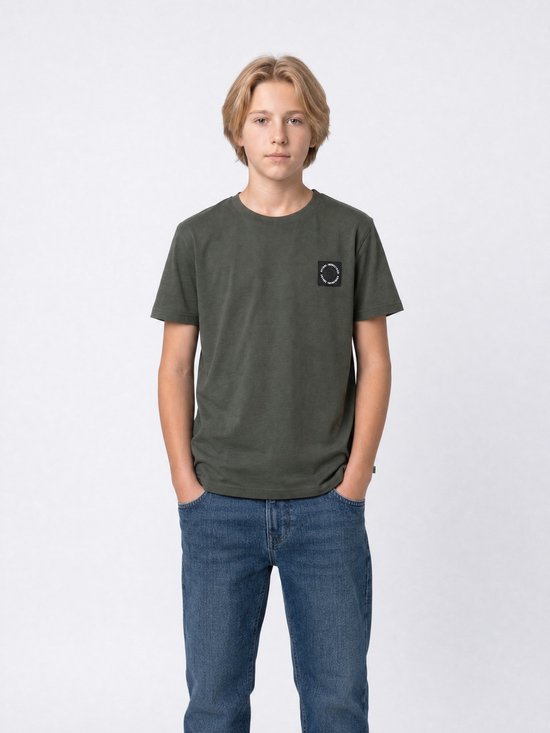 Jongen staat recht vooruit in een donkergroen T-shirt met 'PETROL INDUSTRIES' logo en blauwe jeans.