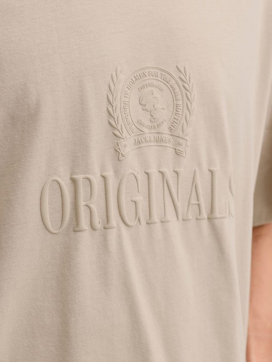 Close-up van de opdruk "ORIGINALS" in reliëf op een lichtbruine T-shirt.