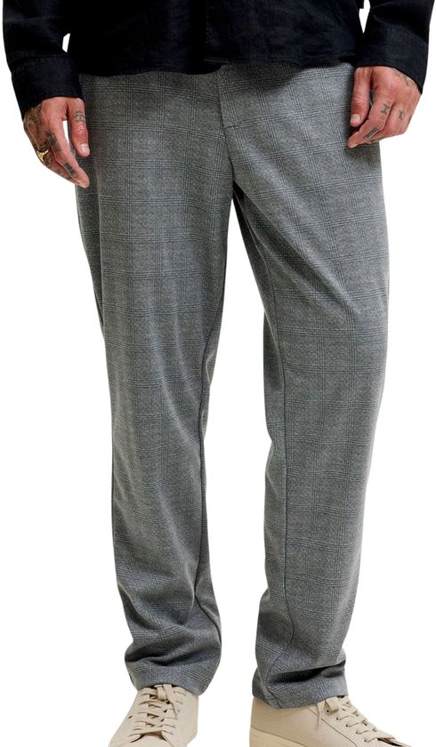 Model draagt een grijze pantalon met ruitpatroon, zwarte top en beige sneakers.