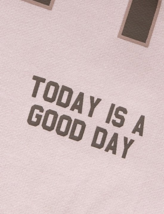 Close-up van de tekst "TODAY IS A GOOD DAY" op een lichtroze sweater.