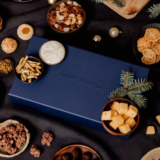 Een open blauwe borrelbox met kaas, worst, crackers, noten, dip en dennentakken.