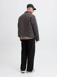 Achteraanzicht: model in zwarte wide-leg joggingbroek met achterzak, getextureerde jas en pet.