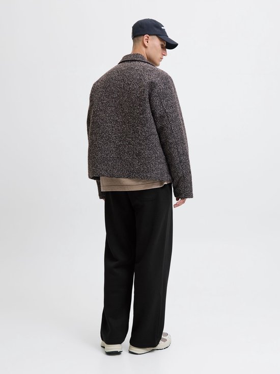 Achteraanzicht: model in zwarte wide-leg joggingbroek met achterzak, getextureerde jas en pet.