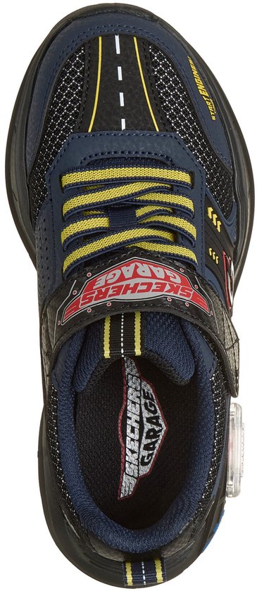 De bovenkant van de sneaker toont een wegpatroon op de neus, gele en blauwe accenten, en het "SKECHERS GARAGE" logo.