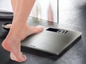 Balance numérique argentée Soehnle avec surface en acier inoxydable brossé. Un pied est sur la balance, l'écran affiche "0.0".