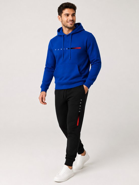 Man loopt in een blauwe hoodie met 'PARIS' tekst en rode/zwarte streepjes, en een zwarte joggingbroek met 'PARIS' op de zijkant.