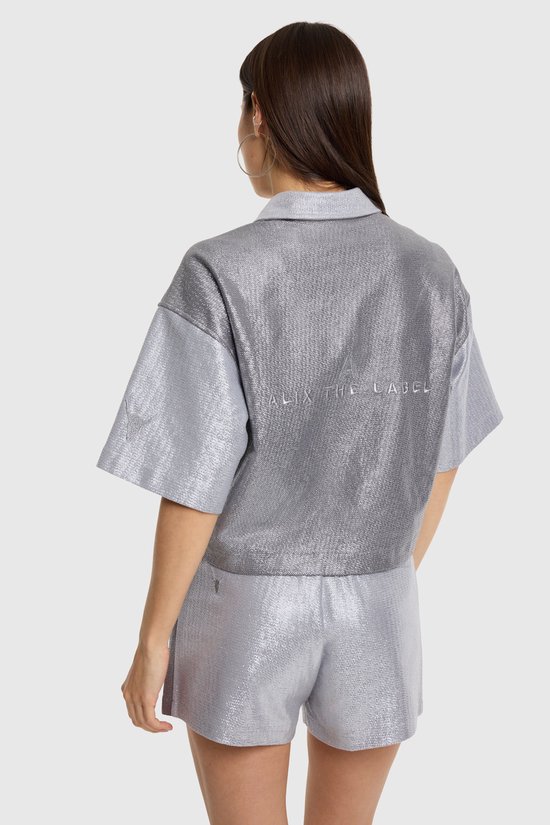De achterkant van een zilverkleurig, glanzend cropped overhemd met korte mouwen, met 'ALIX THE LABEL' op de rug.