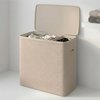 Beige wasmand met drie vakken en deksel, staand naast een witte wasmachine.