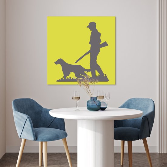 Poster met jager en hond op gele achtergrond, hangend boven een witte tafel met stoelen in een eetkamer.