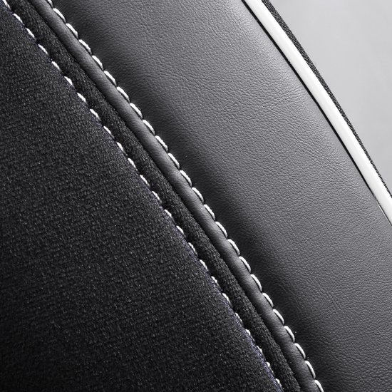 Detail van de naad tussen de zwarte stof met ruitpatroon en het gladde zwarte materiaal van een autostoelhoes, met witte stiksels.