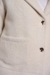 Gros plan sur la veste en tricot blanc cassé avec des boutons dorés et une poche plaquée.