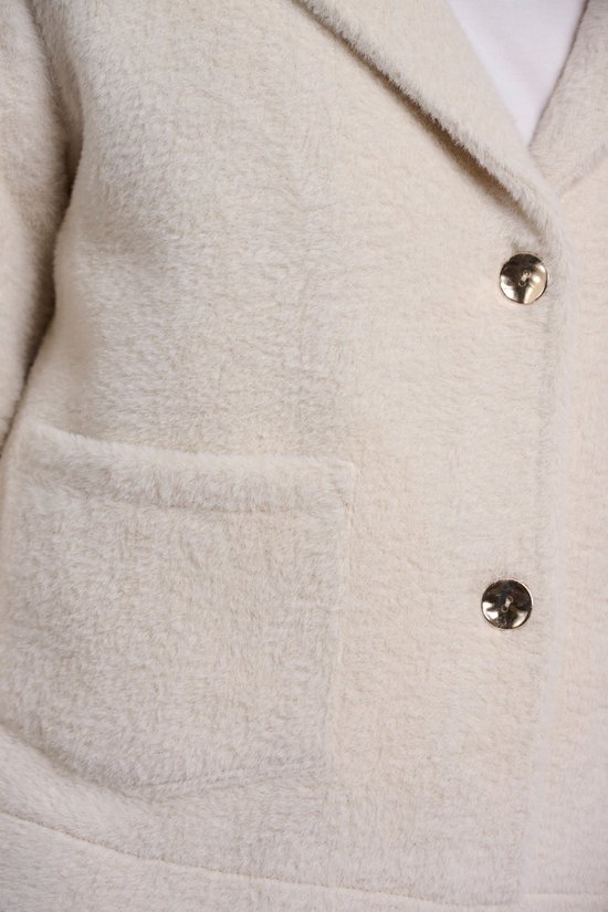 Gros plan sur la veste en tricot blanc cassé avec des boutons dorés et une poche plaquée.