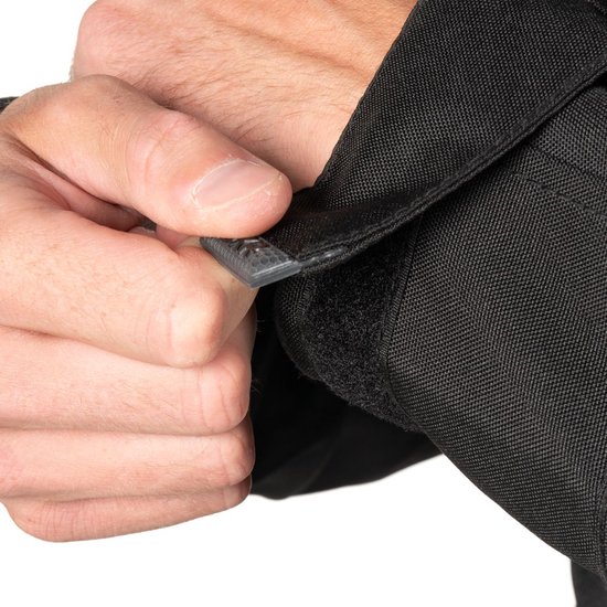 Hand sluit klittenband op zwarte jas, dichtbij.