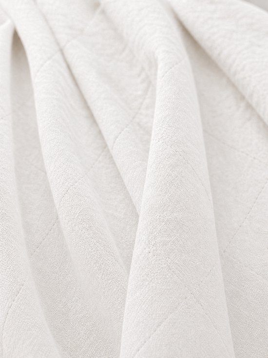 Detail van een witte, gewatteerde sprei met ruitpatroon.