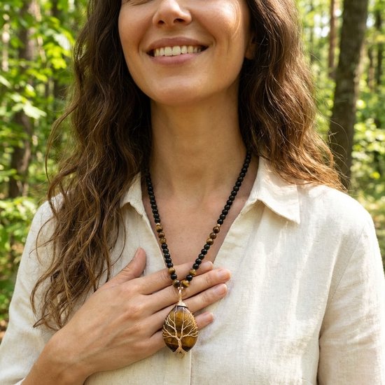 Vrouw met beige blouse draagt een lange ketting met zwarte en tijgeroogkleurige kralen en een hanger van tijgeroog in boomvorm.