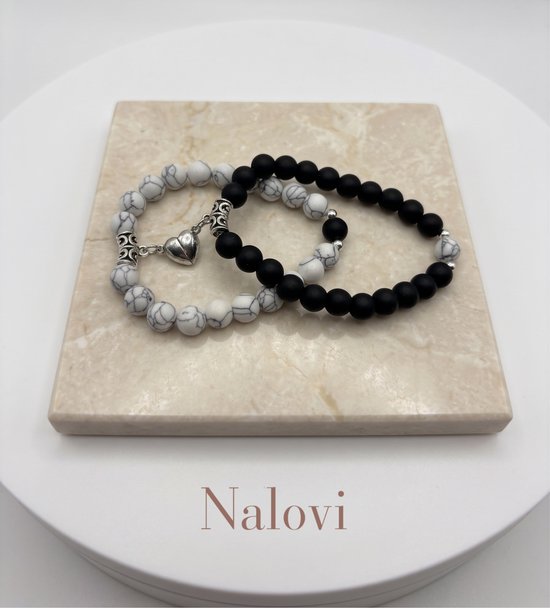 Twee armbanden, één met witte kralen met grijze lijnen en één met zwarte kralen. Beide met zilverkleurige bedels en een hartvormige magneetsluiting.