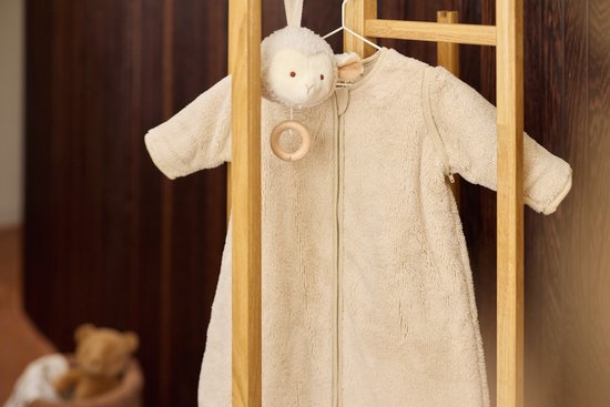 Beige teddy slaapzak met mouwen hangend aan een houten rek met schaapjesknuffel.