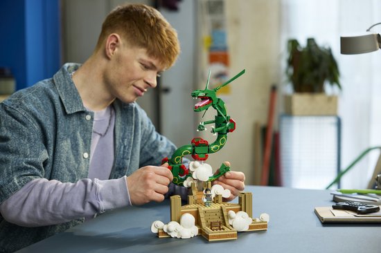 Close-up van een jongeman die een groene LEGO Rayquaza met rode accenten, een bruin altaar en figuurtje vasthoudt.