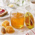Glazen pot met gouden honing, met druipende honing, naast honingraten en een honinglepel.