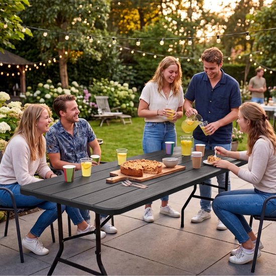 Zes personen aan een zwarte, inklapbare tafel in de tuin met eten en drinken.