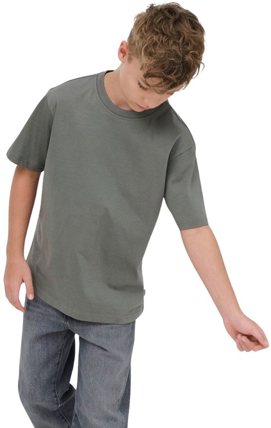 Jongen met blond haar draagt een effen donkergrijs T-shirt en spijkerbroek, kijkt naar beneden.