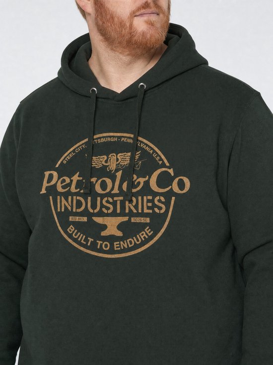 Close-up van man in donkergroene hoodie met gouden merkprint 'Petrol & Co Industries' op de borst.