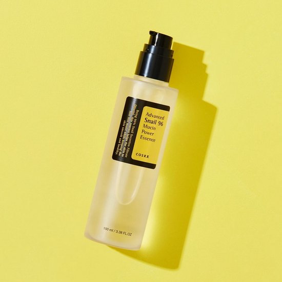 COSRX Advanced Snail 96 Mucin Power Essence, een heldere vloeistof in een matte fles met zwarte pompdispenser, op gele achtergrond.