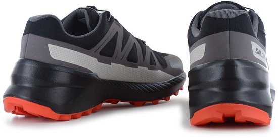 Achterkant van zwarte Salomon trailrunningschoen met grijze details en oranje zool. Reflecterende streep.