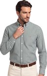 Man met een groen met wit gestreept katoenen Gant overhemd, witte broek en bruine riem.