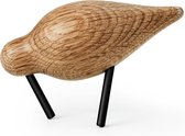 Houten vogelbeeldje met een gebogen, organische vorm en twee zwarte metalen pootjes.